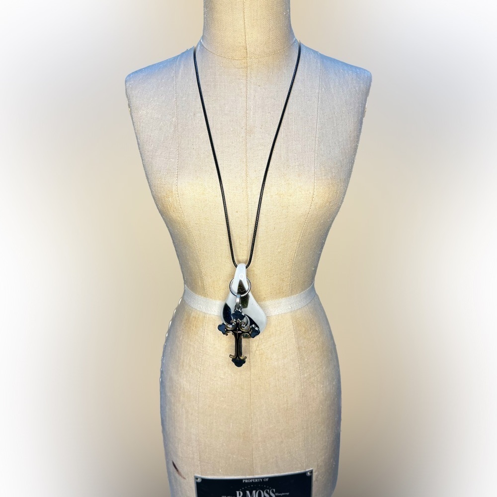Glass pendant with ornate cross pendant in front on black rope chain.